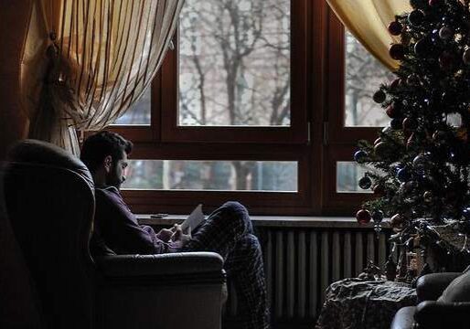 Individual reading by a window next to a Christmas tree